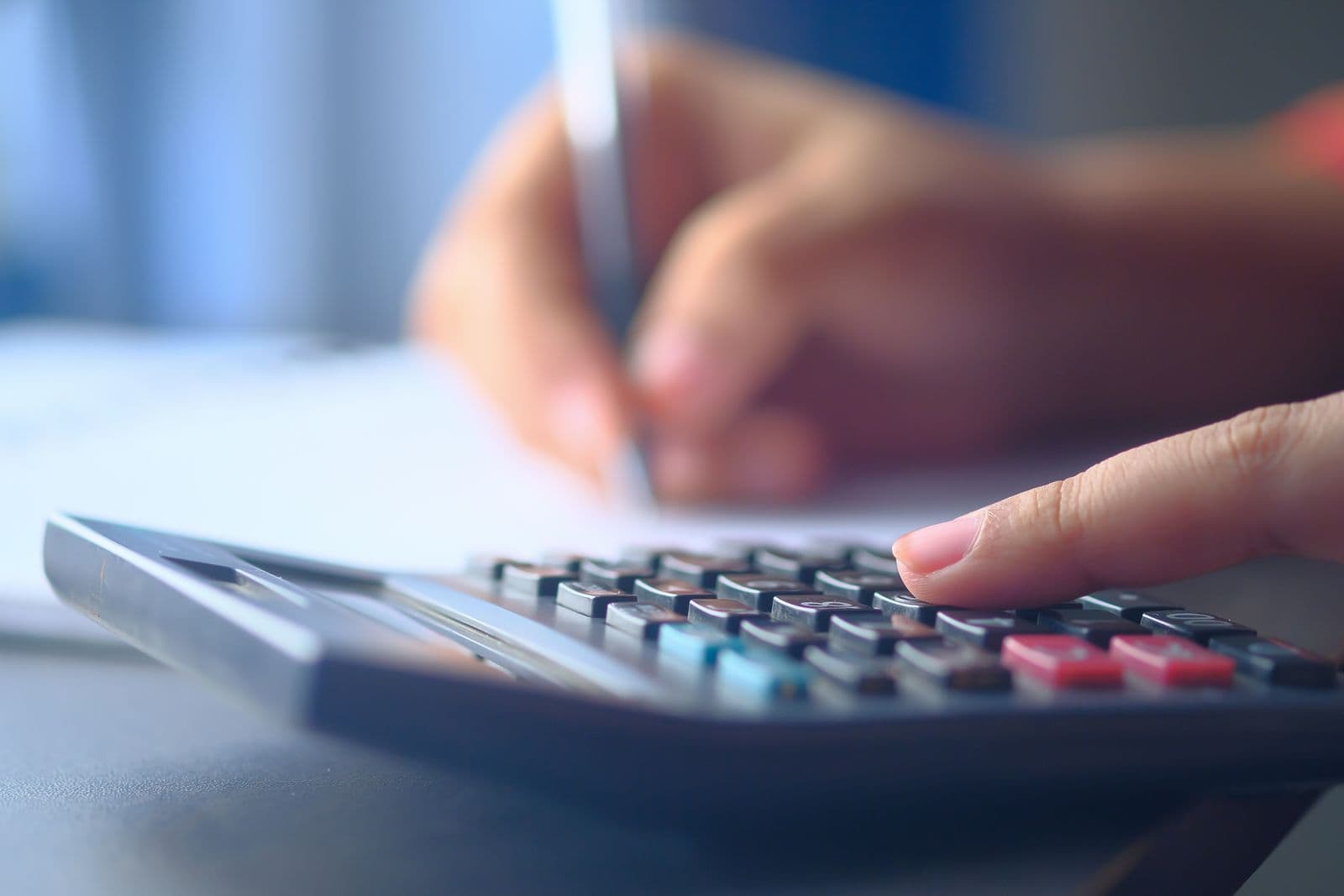A person reviewing budget figures on paper beside a calculator and laptop