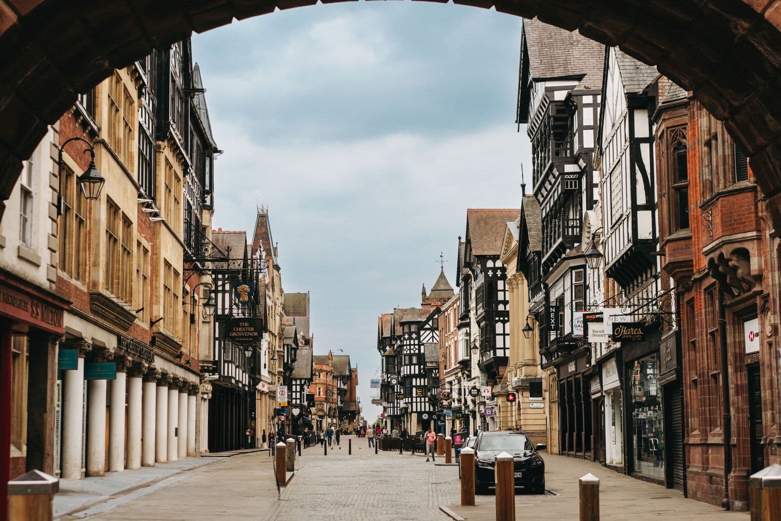 A cobbled pedestrian street framed by a stone arch, black-and-white timbered upper storeys receding into the distance