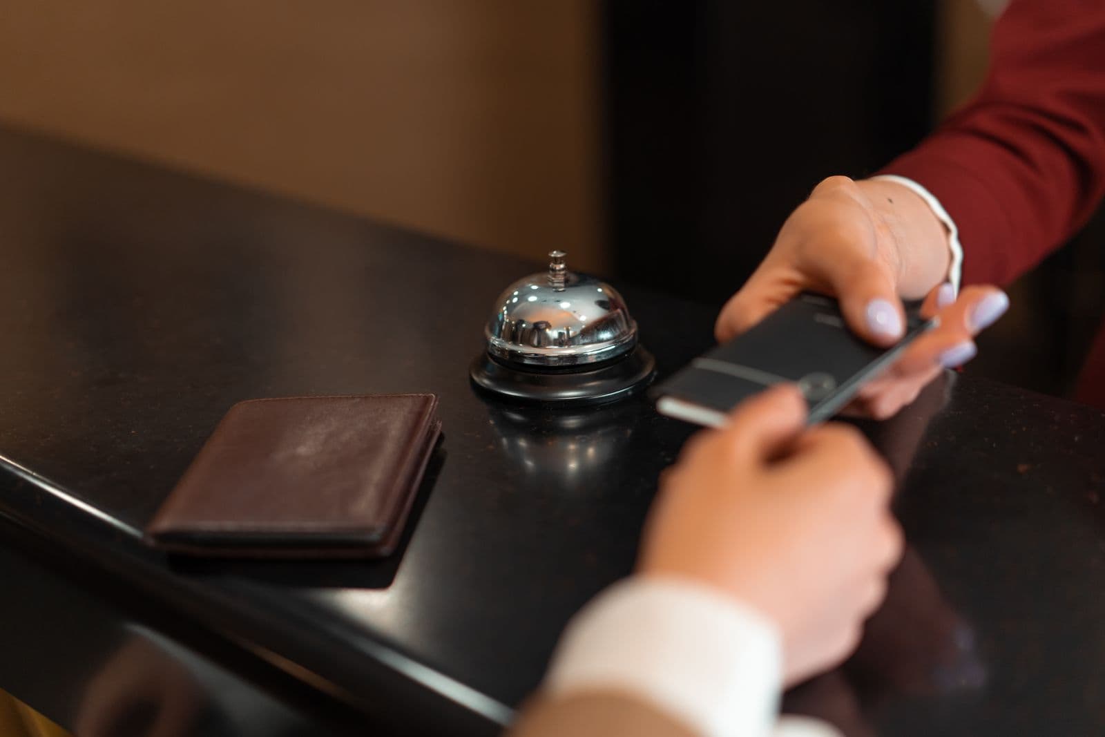 A phone passed across a hotel reception counter beside a service bell and a leather folder