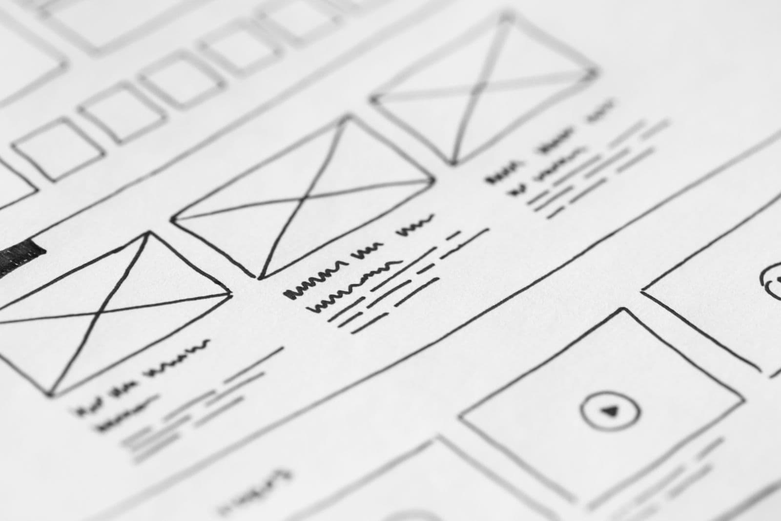A hand-drawn paper wireframe of a page layout, crossed boxes standing in for images and squiggles for text