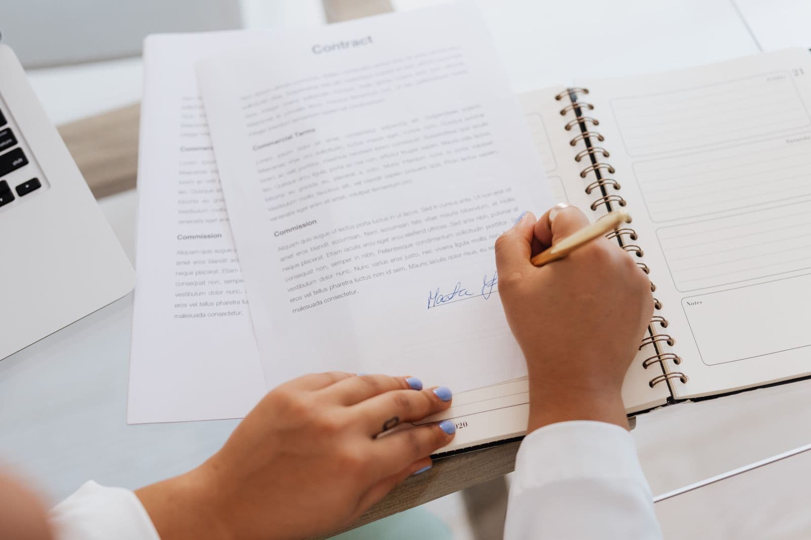A printed contract on a desk with a pen, alongside a laptop open to a document review screen