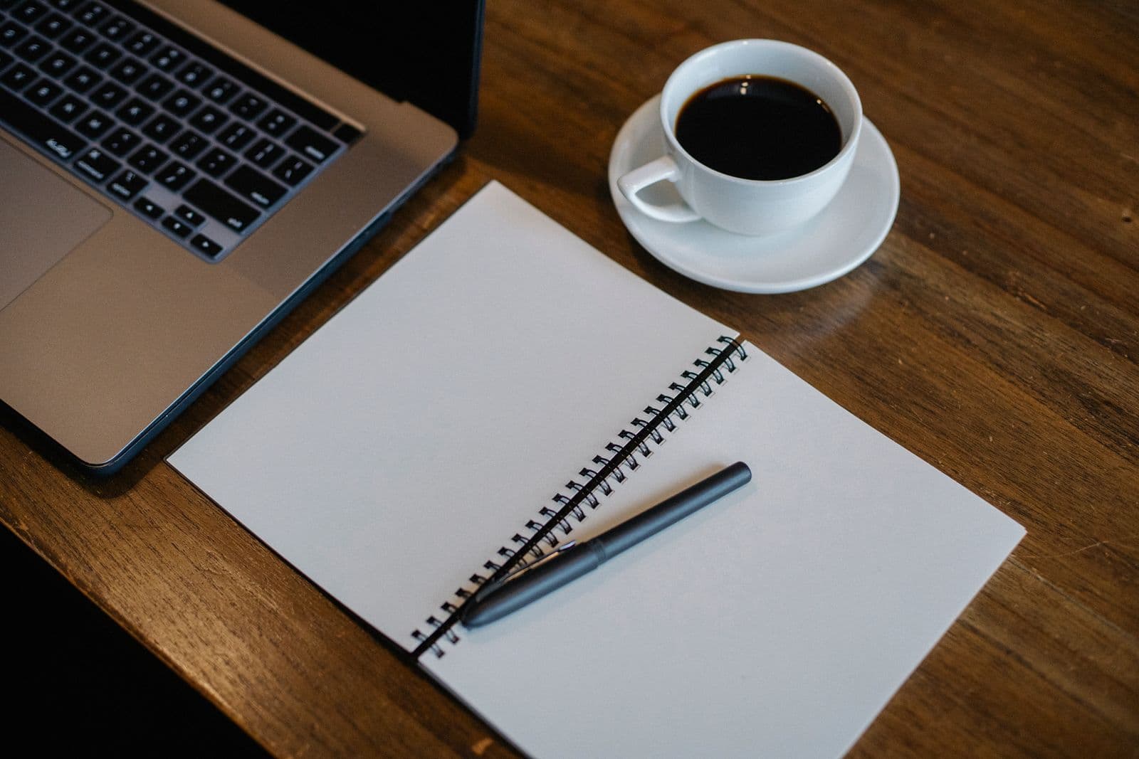 A person planning their week on a laptop and phone at a desk with a notebook and coffee