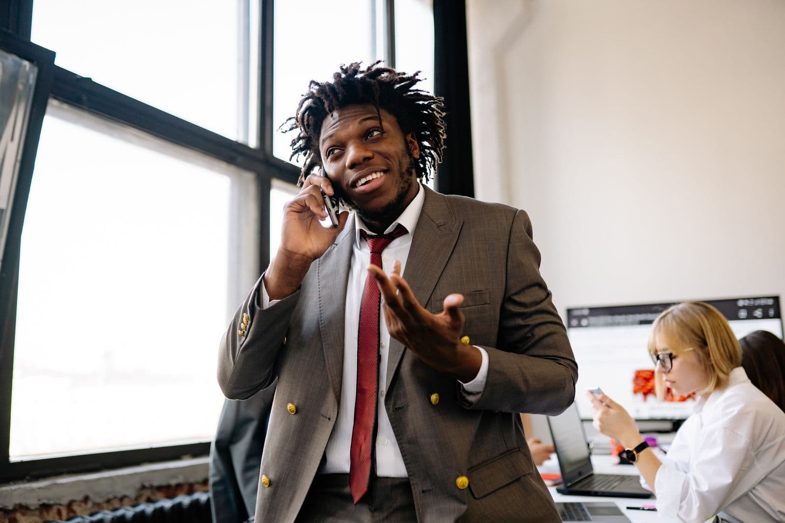 Smiling man in a suit gesturing while talking on his mobile phone in an office