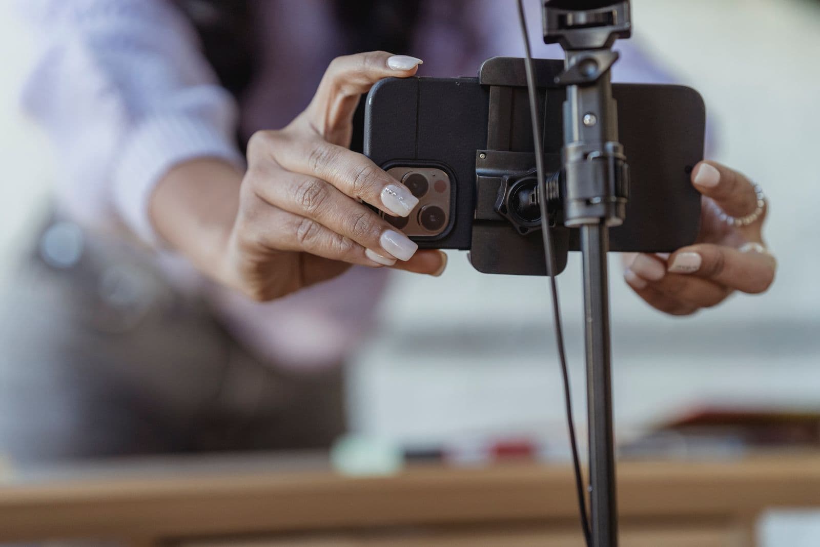 Hands clamping a smartphone into a tripod mount above a blurred desk