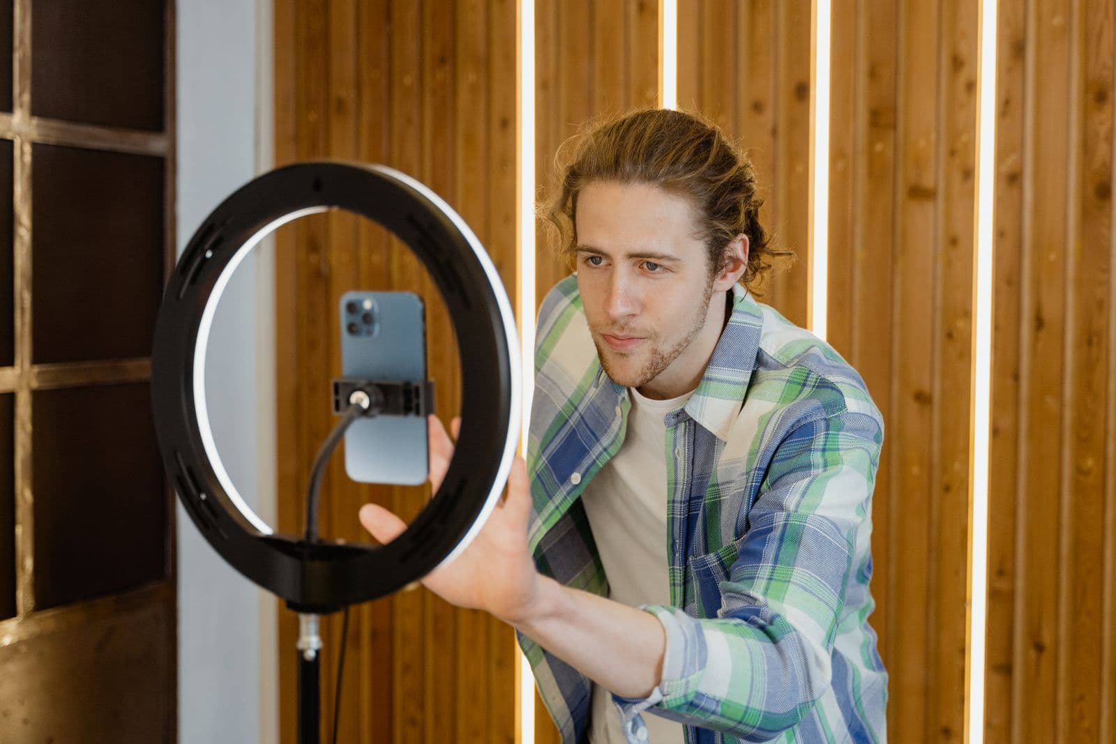 Man adjusting a vertically mounted phone inside a lit ring light against a wooden wall