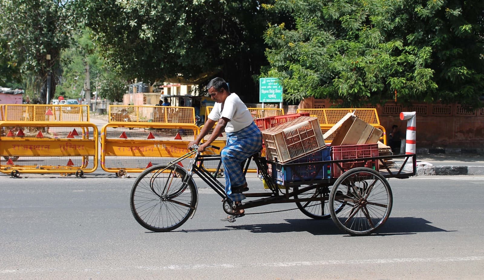 A man pedalling a cargo cycle-rickshaw loaded with crates along a city street