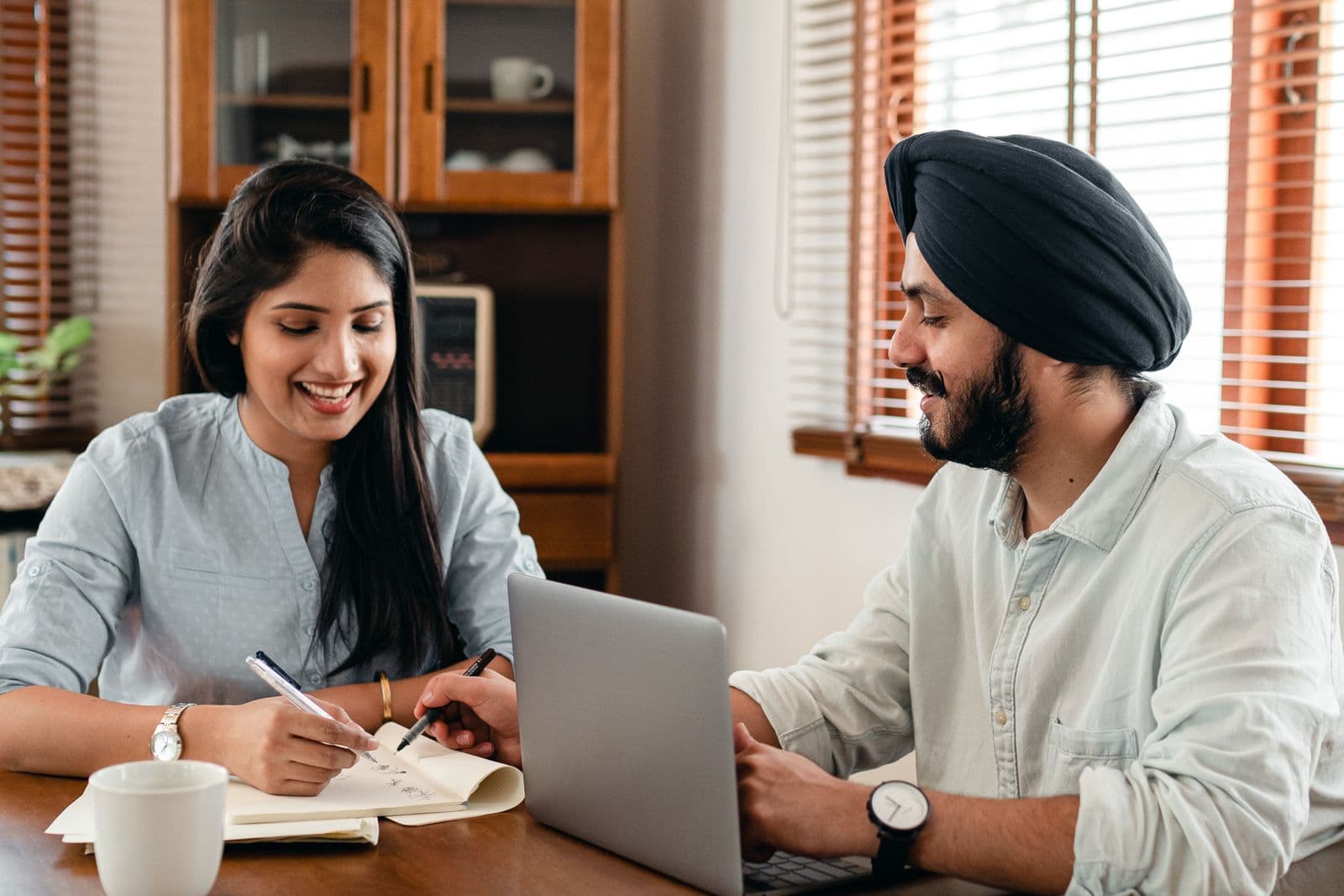 A woman sketching in a notebook beside a man in a turban working at a laptop